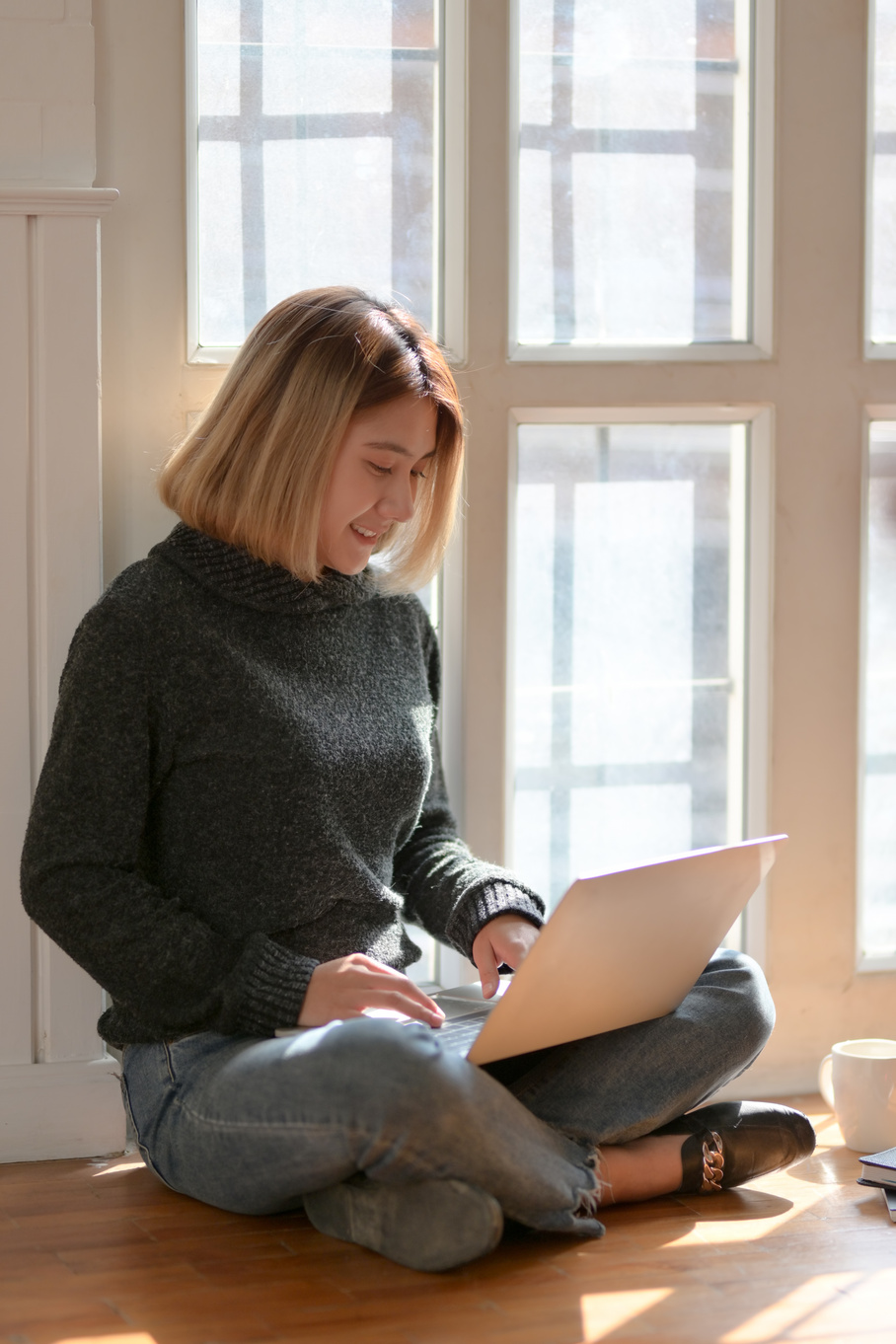 Woman in Gray Sweater Sitting on Wooden Floor Typing on Portable Computer